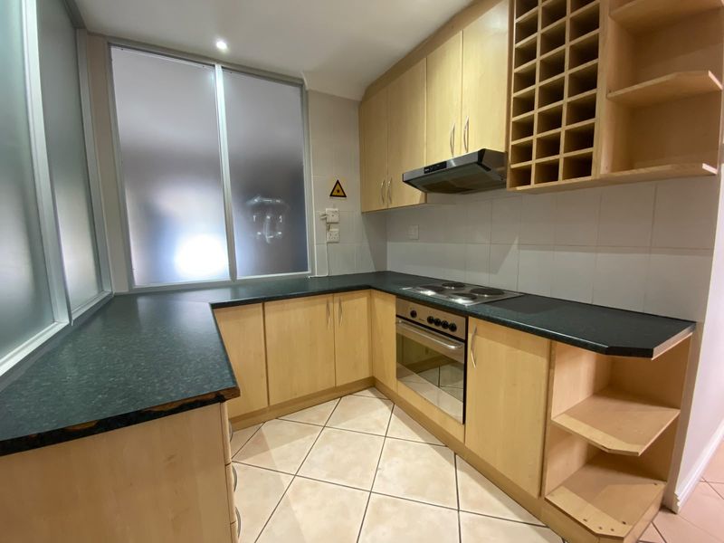 A functional kitchen featuring light wood cabinetry, dark laminate countertops, built-in oven, electric hob, and tiled flooring.
