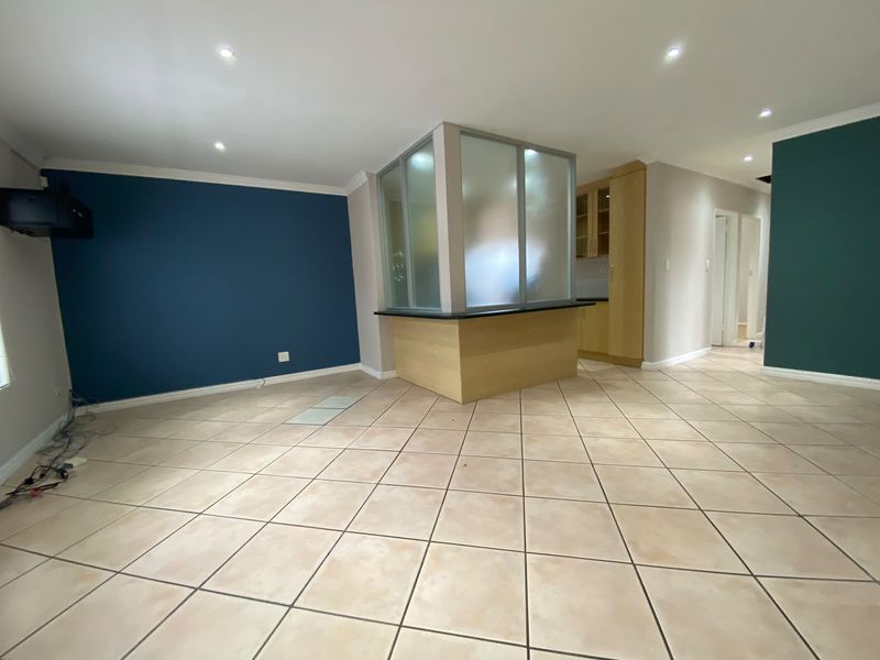 Spacious open-plan living area featuring tiled flooring, recessed lighting, and a central kitchen partition with a breakfast counter.
