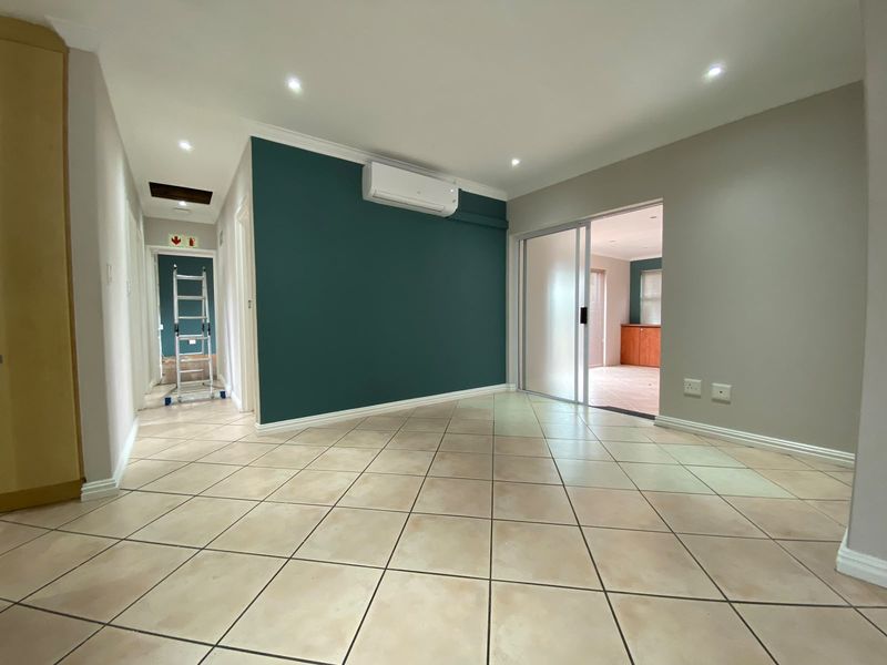 An empty living area featuring tiled flooring, recessed lighting, a wall-mounted air conditioning unit, and a sliding glass door leading to an adjacent room.