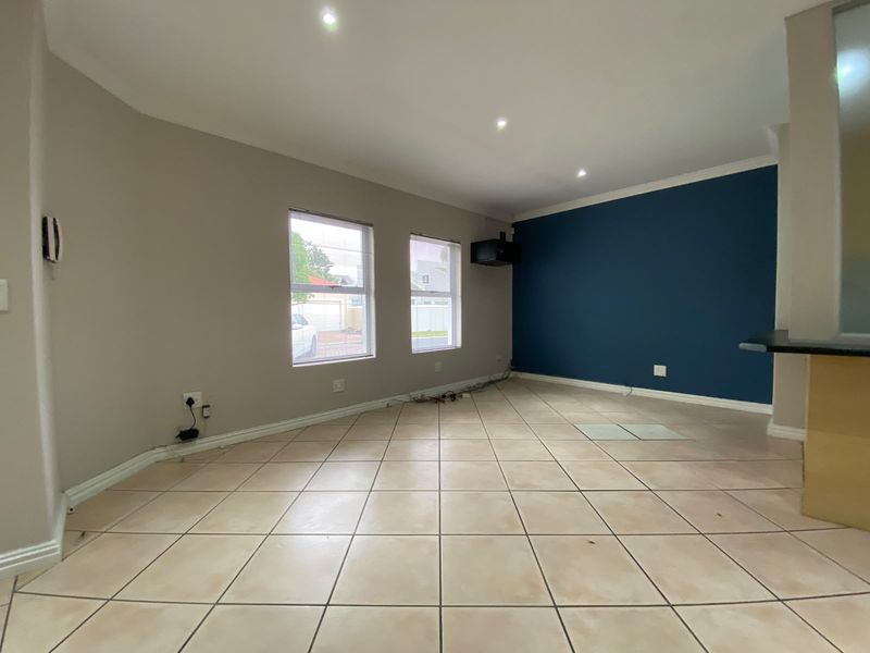 An empty living room featuring tiled flooring, recessed downlights, and a blue accent wall, with an adjacent breakfast bar area.
