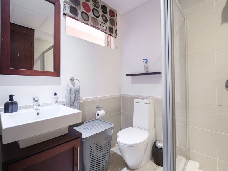 A functional bathroom featuring a vanity cabinet with a basin, a toilet, and a glass-enclosed shower with neutral wall tiling.