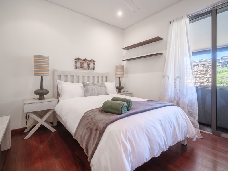 A well-maintained bedroom featuring rich hardwood flooring, recessed lighting, and direct access to a private balcony through large sliding glass doors.