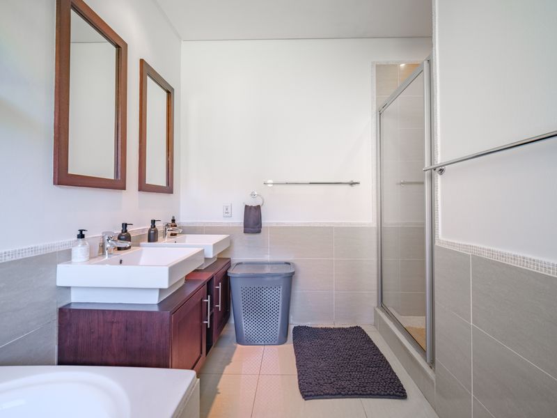 Modern bathroom featuring a double vanity with dark wood cabinetry, wall-mounted mirrors, and a glass-enclosed shower with neutral wall and floor tiling.