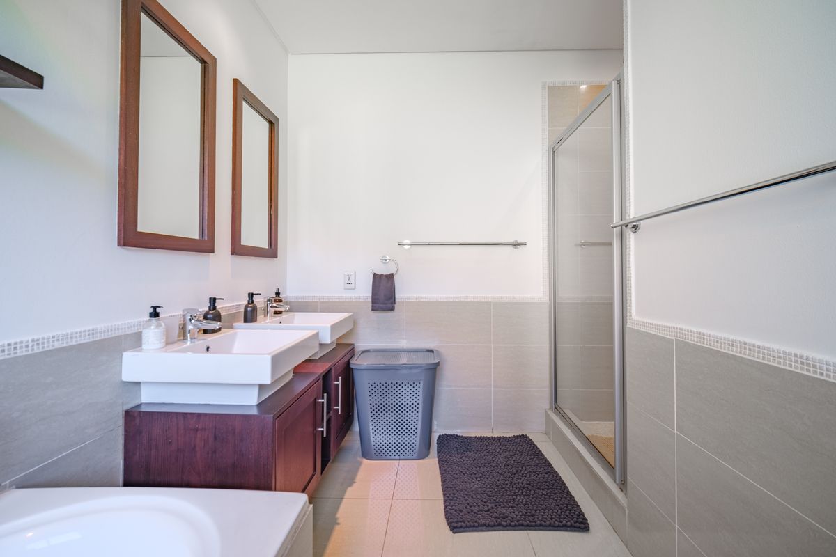 Modern bathroom featuring a double vanity with dark wood cabinetry, wall-mounted mirrors, and a glass-enclosed shower with neutral wall and floor tiling.