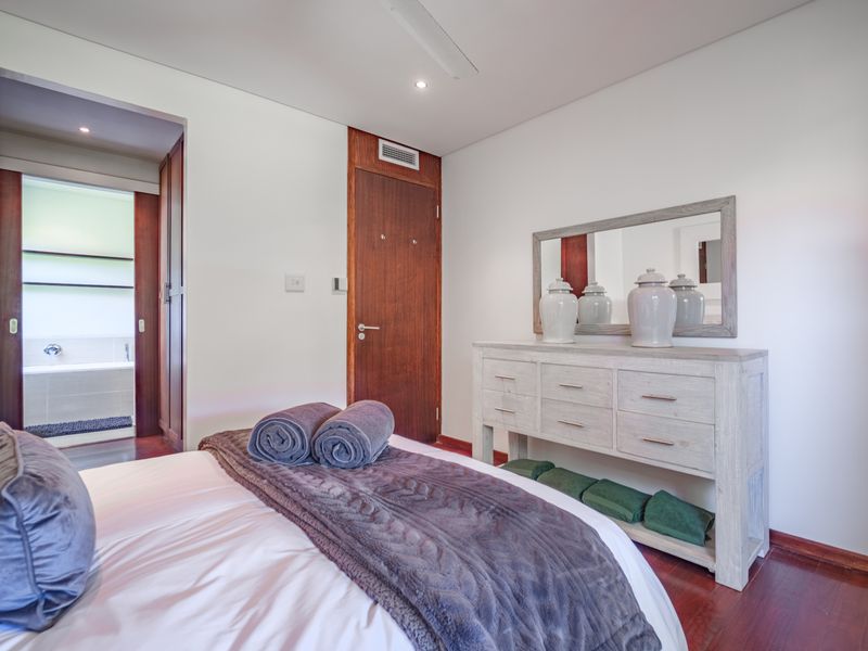 A well-maintained bedroom featuring hardwood flooring, recessed lighting, and direct access to an en-suite bathroom with a neutral color palette.