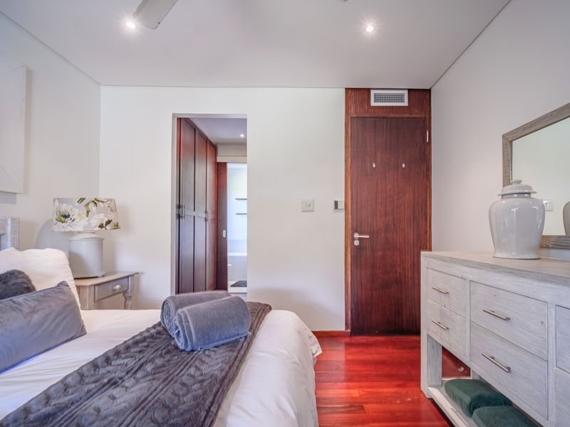 A well-maintained bedroom featuring polished hardwood flooring, recessed lighting, and a solid timber door leading to an en-suite bathroom.