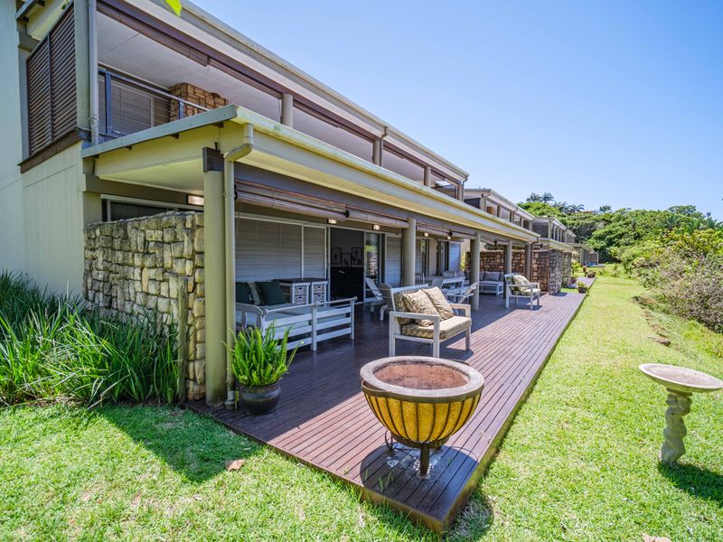 Spacious covered patio featuring timber decking, stone accent walls, and direct access to the garden through large sliding glass doors.