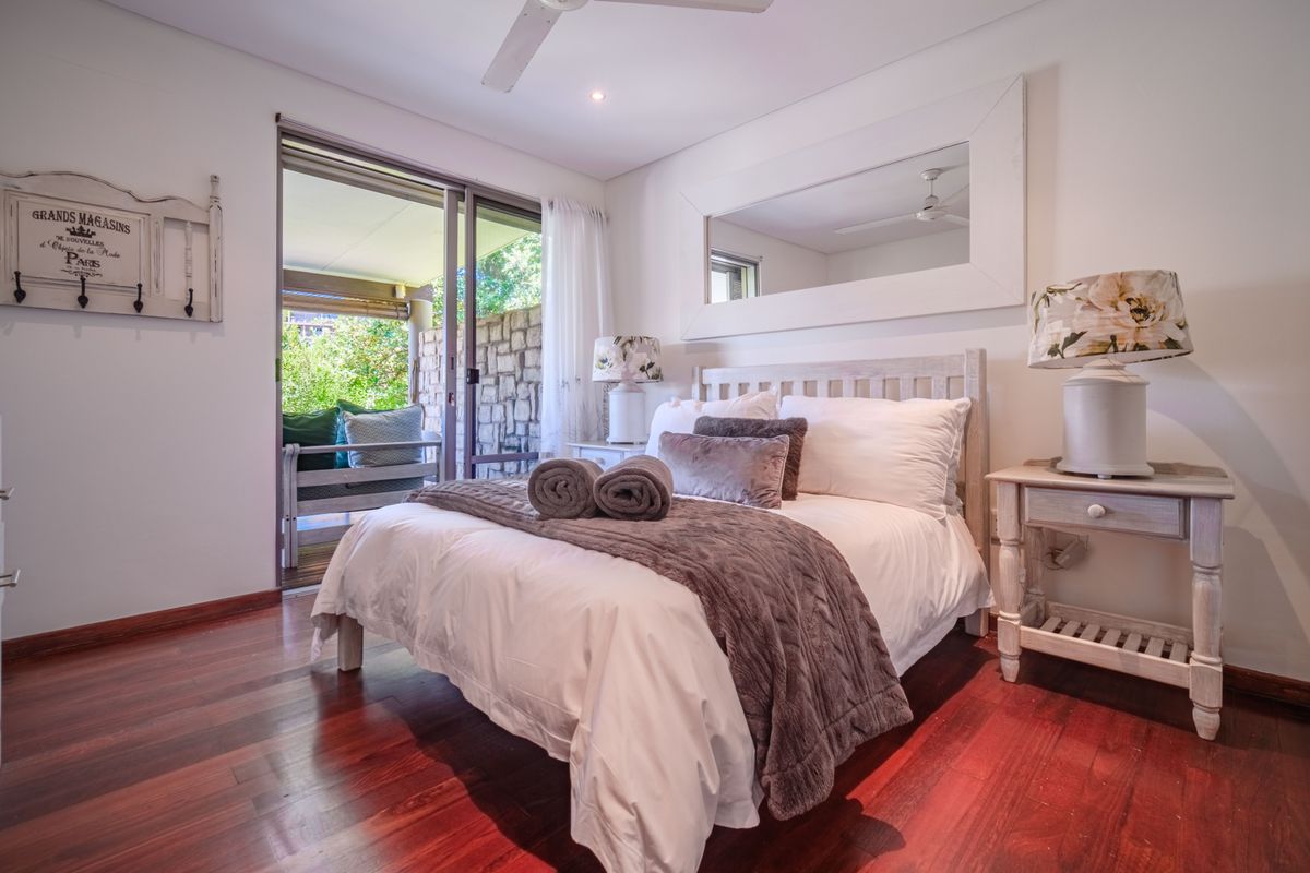 A well-maintained bedroom featuring rich hardwood flooring, a ceiling fan, and a sliding glass door providing direct access to an outdoor patio area.