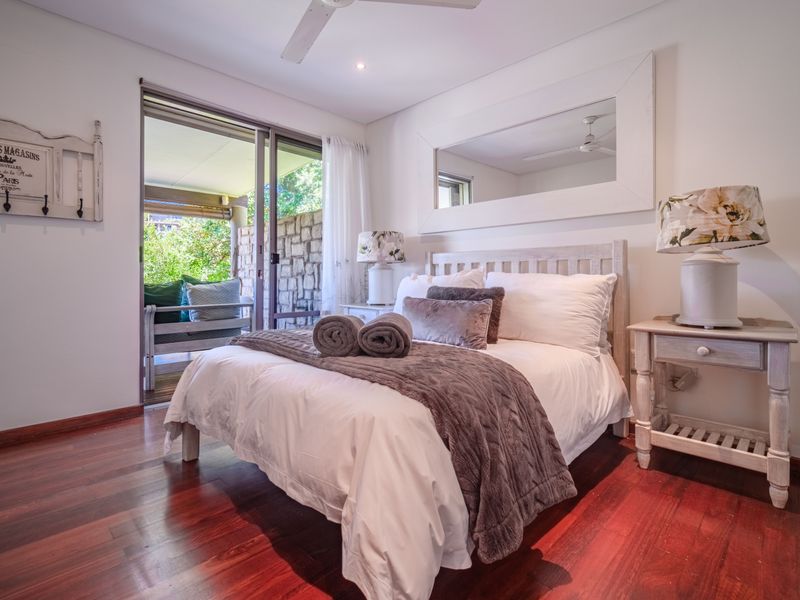 A well-maintained bedroom featuring rich hardwood flooring, a ceiling fan, and a sliding glass door providing direct access to an outdoor patio area.