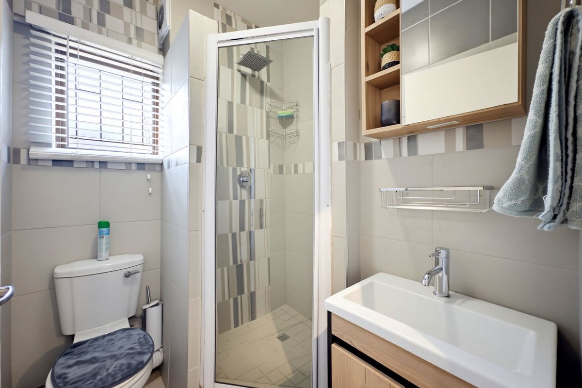 A modern bathroom featuring a glass-enclosed shower, a vanity with a basin, a wall-mounted medicine cabinet, and neutral tiled finishes.