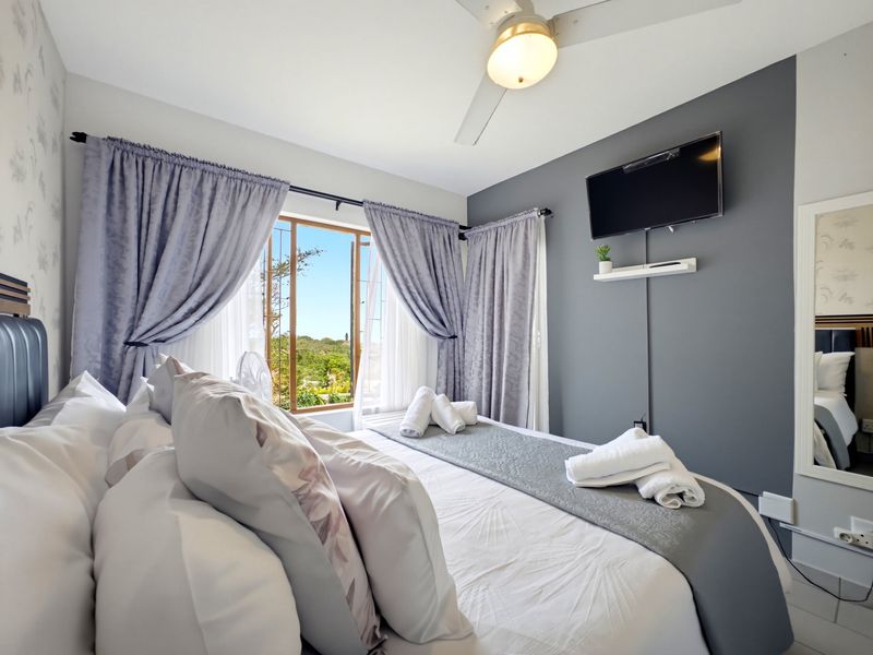 A well-maintained bedroom featuring a ceiling fan, wall-mounted television, and large windows with security bars, offering a bright and comfortable living space.