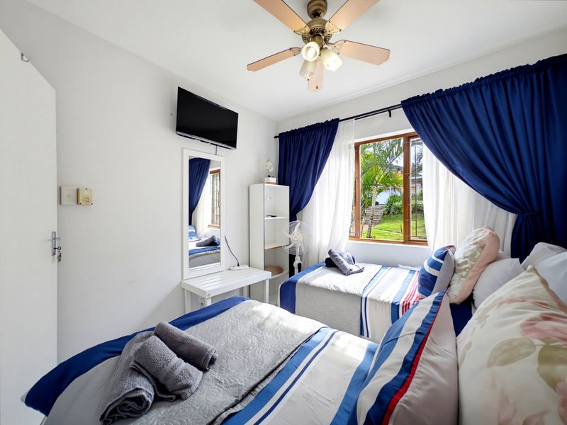 A bedroom featuring a ceiling fan, timber-framed window with garden views, and built-in shelving, providing a functional and comfortable living space.