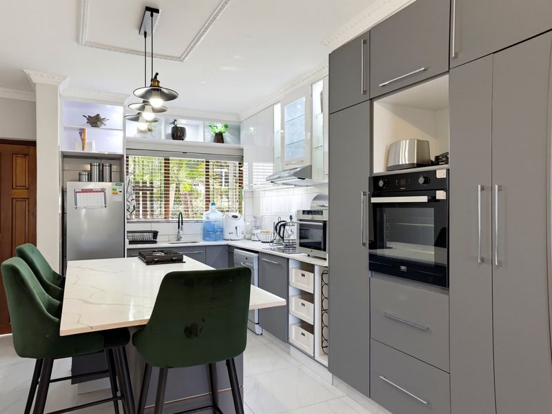 Modern kitchen featuring grey cabinetry, stone-topped island with seating, built-in oven, and elegant cove ceiling detailing.