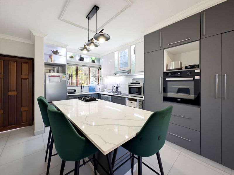 Modern kitchen featuring a large quartz island, built-in oven, gas hob, sleek grey cabinetry, and tiled flooring with elegant ceiling molding.
