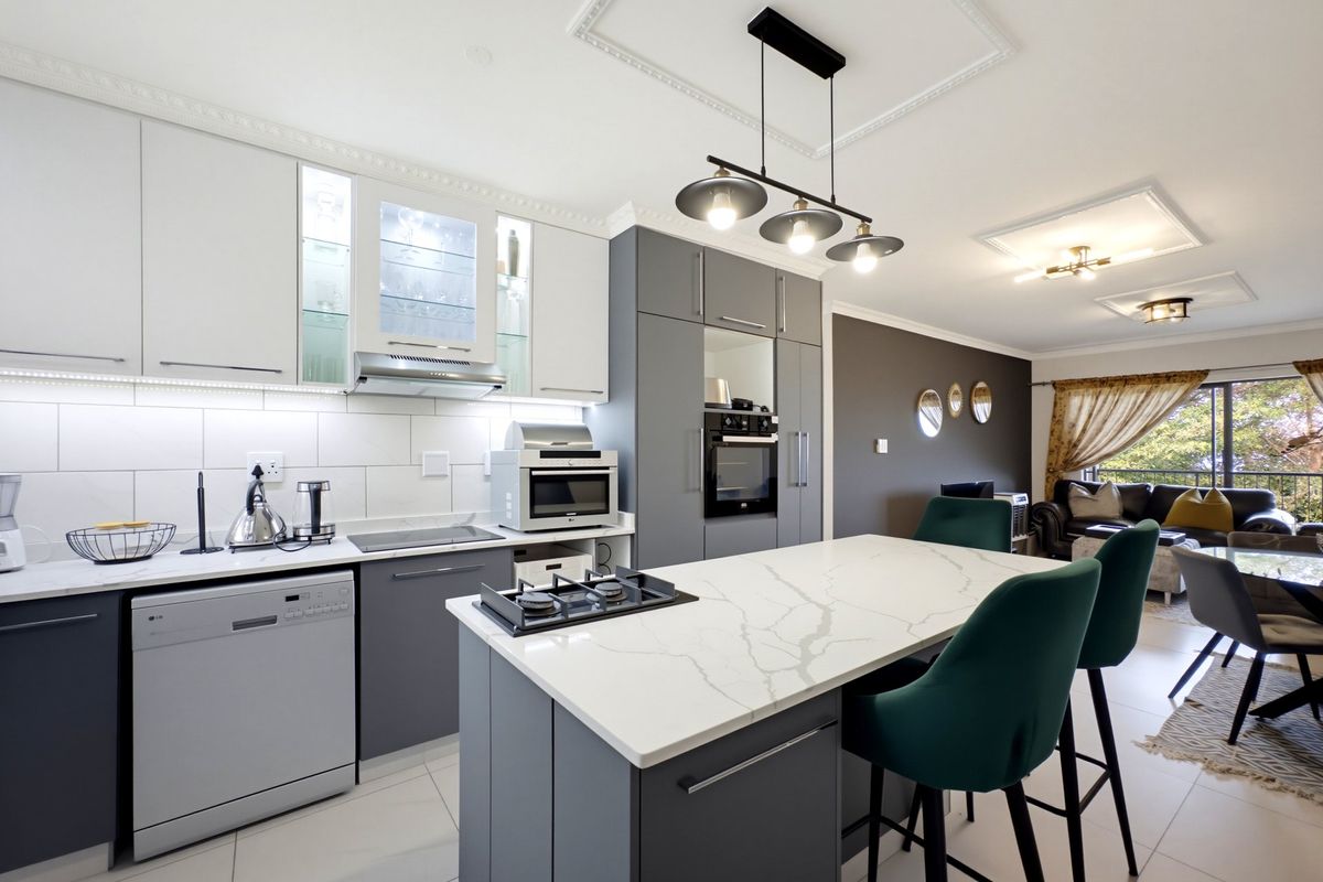 Modern open-plan kitchen featuring a central island with gas cooktop, sleek cabinetry, integrated appliances, and elegant pendant lighting, flowing into the living area.