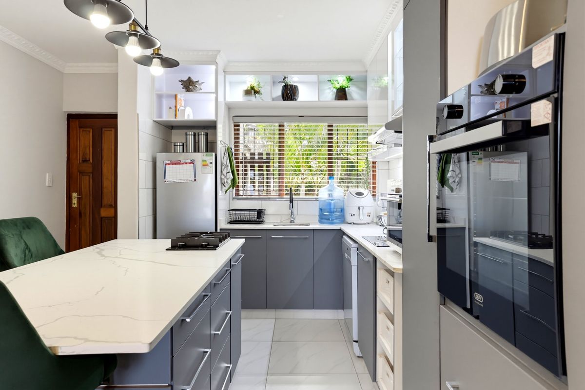 Modern kitchen featuring a central island with a gas hob, sleek grey cabinetry, stone countertops, built-in oven, and contemporary pendant lighting.