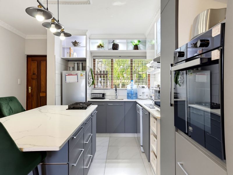 Modern kitchen featuring a central island with a gas hob, sleek grey cabinetry, stone countertops, built-in oven, and contemporary pendant lighting.