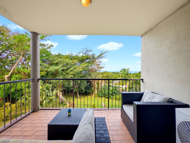 A covered balcony featuring tiled flooring, a metal balustrade, and scenic views of the surrounding greenery and distant ocean.