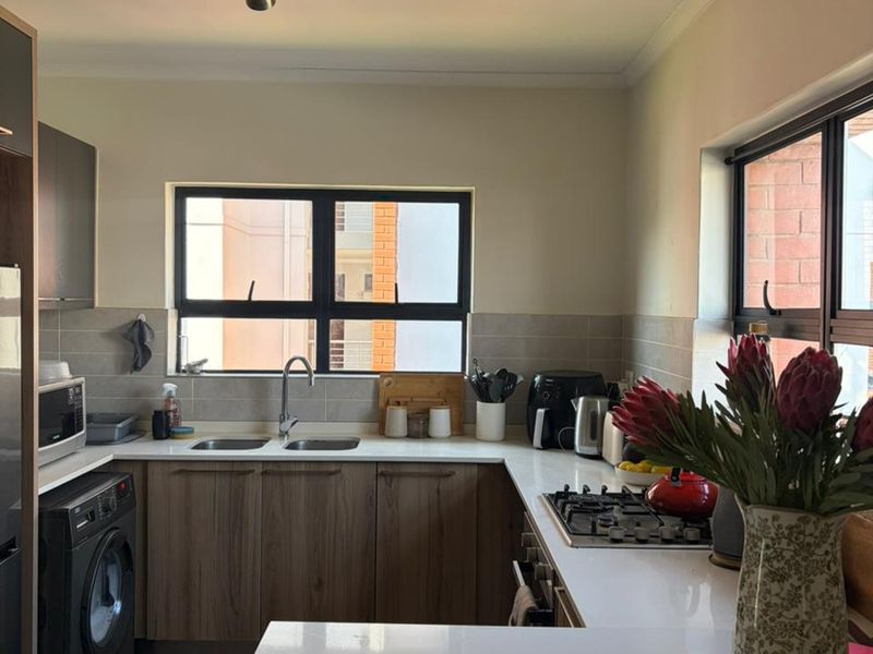 Modern kitchen featuring wood-finish cabinetry, stone countertops, a gas hob, built-in oven, and a double basin sink with tiled backsplash.
