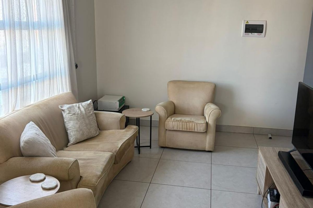 A living room featuring neutral tiled flooring and a wall-mounted electrical distribution board, offering a functional and well-lit space.