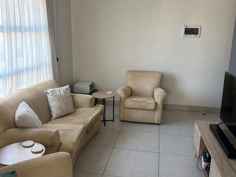 A living room featuring neutral tiled flooring and a wall-mounted electrical distribution board, offering a functional and well-lit space.