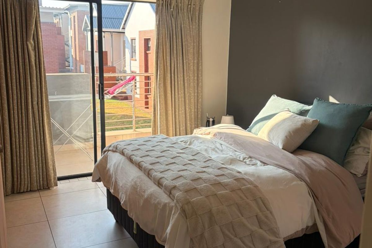 A well-lit bedroom featuring tiled flooring, an accent wall, and a sliding glass door providing access to an outdoor balcony area.