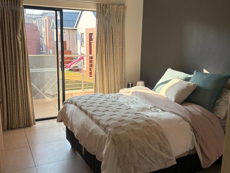 A well-lit bedroom featuring tiled flooring, an accent wall, and a sliding glass door providing access to an outdoor balcony area.