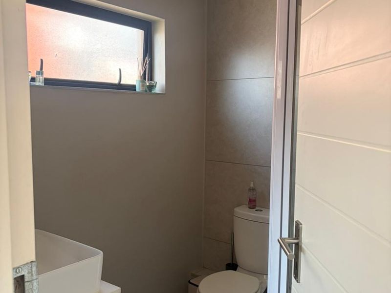 A modern bathroom featuring a vessel sink vanity, a toilet, and a shower enclosure with neutral wall and floor tiling.