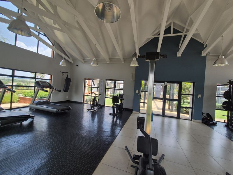 Spacious gym facility featuring vaulted ceilings with exposed rafters, a mix of rubber and tiled flooring, and large windows providing ample natural light.