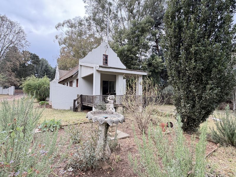 Rear view of a cottage-style house featuring a timber deck, gabled roof architecture, and a spacious garden setting.