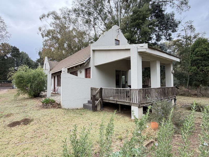 Rear view of a house featuring a gabled roof, a covered patio area, and an elevated wooden deck set within a large garden.