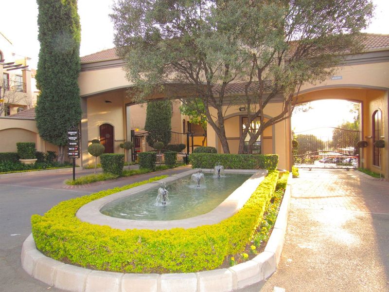The entrance to the apartment complex features a well-maintained landscaped garden with a central water fountain and secure gated access.