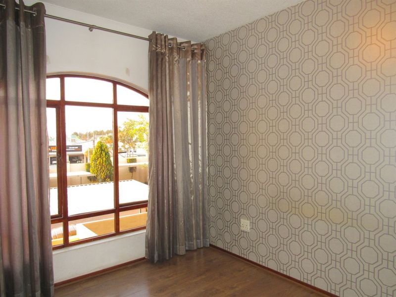An empty bedroom featuring laminate flooring, a distinctive arched window, and a patterned feature wall.