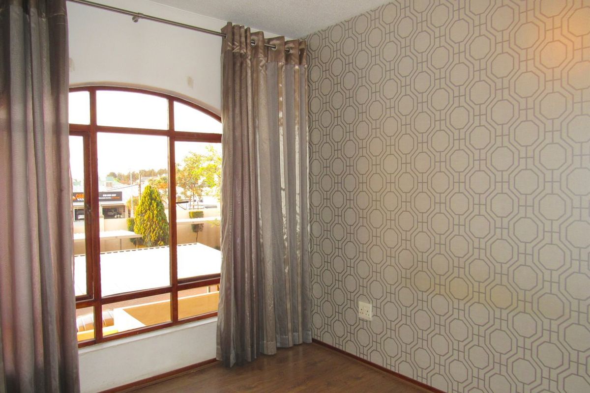 An empty bedroom featuring laminate flooring, a distinctive arched window, and a patterned feature wall.