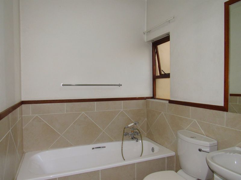 A functional bathroom featuring a bathtub, toilet, and pedestal basin with neutral wall tiling and a wooden dado rail.