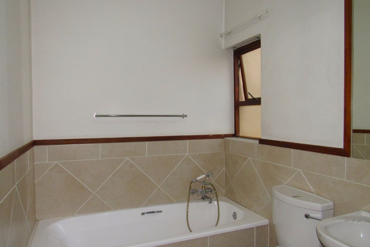 A functional bathroom featuring a bathtub, toilet, and pedestal basin with neutral wall tiling and a wooden dado rail.
