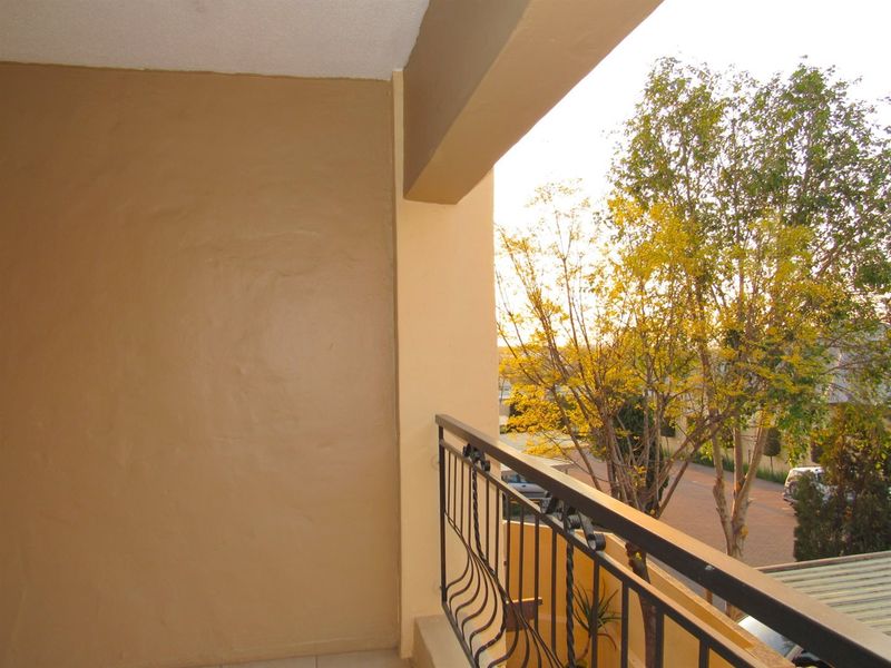 A private balcony featuring a wrought iron balustrade and tiled flooring, offering an elevated view of the surrounding neighborhood and trees.