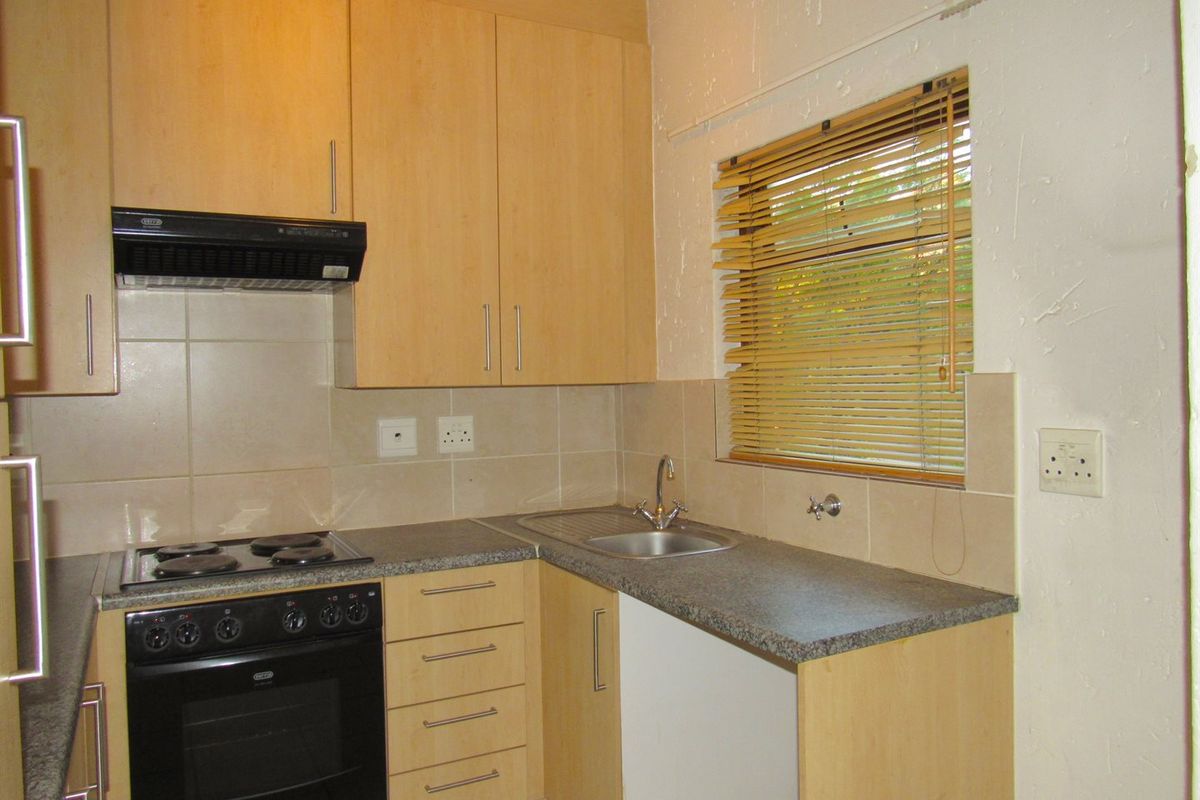 A functional kitchen featuring light wood-finish cabinetry, built-in oven and hob, tiled backsplash, and a stainless steel sink with a window view.