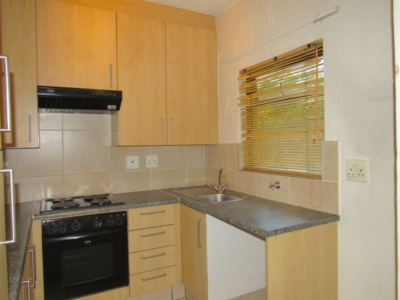 A functional kitchen featuring light wood-finish cabinetry, built-in oven and hob, tiled backsplash, and a stainless steel sink with a window view.