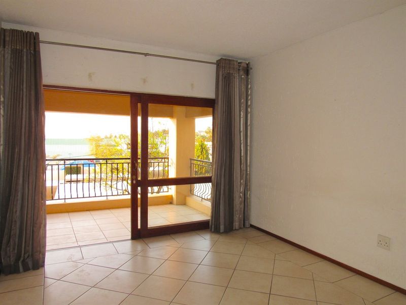 An empty living room featuring tiled flooring and a sliding glass door providing access to a private balcony.