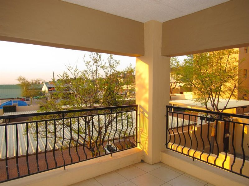 A covered balcony featuring tiled flooring and a decorative wrought iron balustrade, offering an elevated view of the surrounding complex and neighbourhood.
