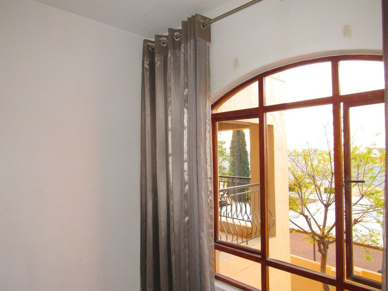 A bright bedroom featuring an arched timber window frame with views of the exterior balcony and surrounding trees.