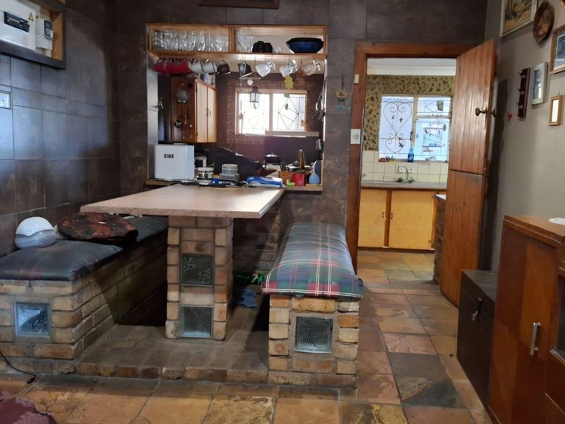 Open plan dining area featuring built-in brick seating and stone tile flooring, with a pass-through window connecting to the adjacent kitchen space.