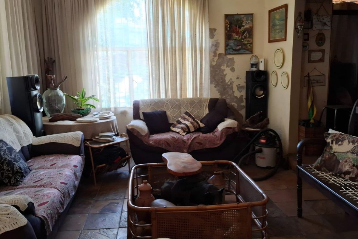 A living room featuring tiled flooring and a large window, currently showing significant wall surface deterioration requiring repair and redecoration.