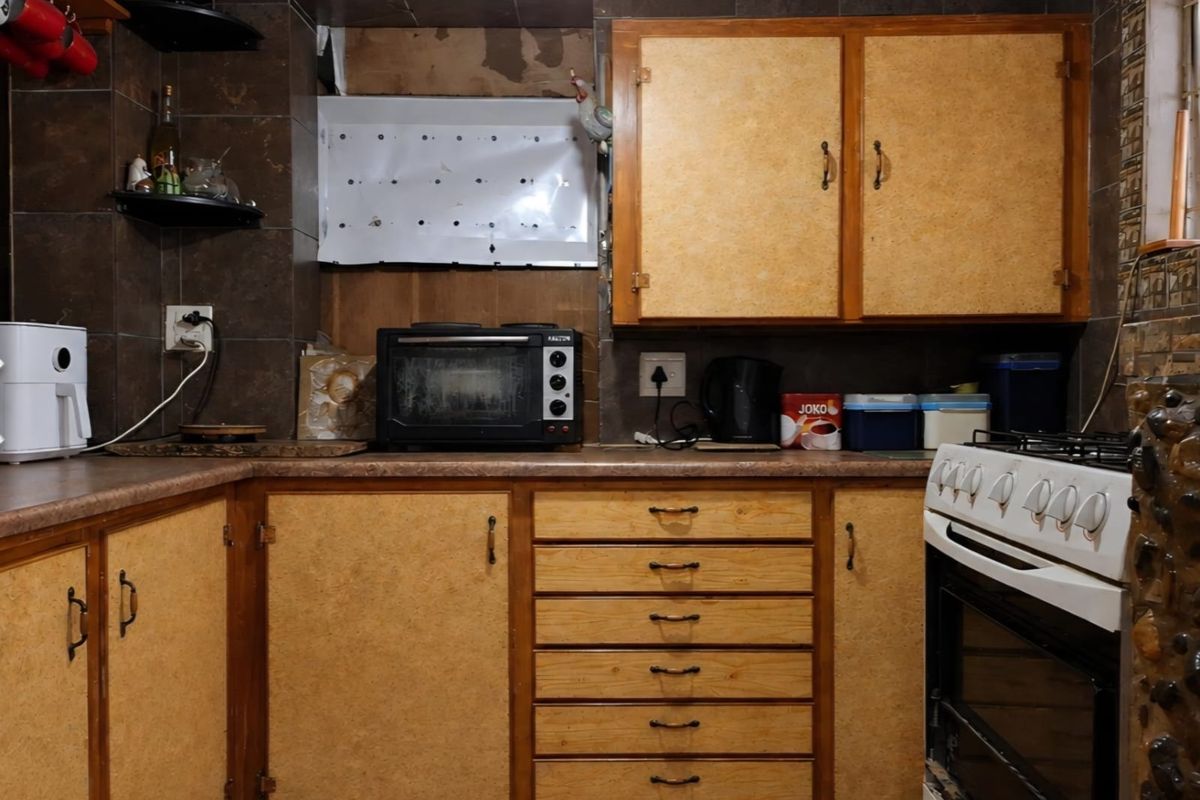 A dated kitchen featuring wooden cabinetry, tiled backsplash, and a gas stove, requiring cosmetic updates to modernize the space.
