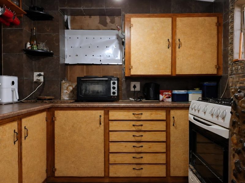 A dated kitchen featuring wooden cabinetry, tiled backsplash, and a gas stove, requiring cosmetic updates to modernize the space.