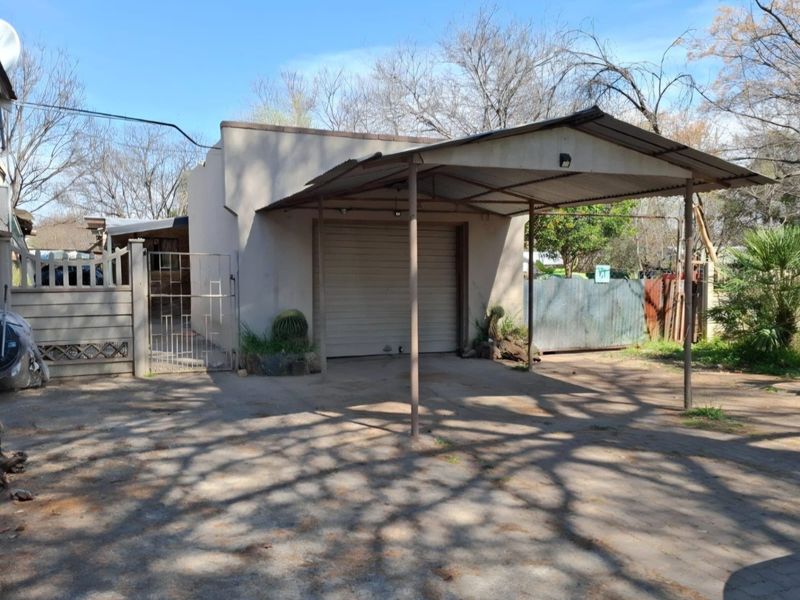 A detached garage structure featuring a roll-up door and an attached metal carport, situated on a paved driveway with perimeter fencing.
