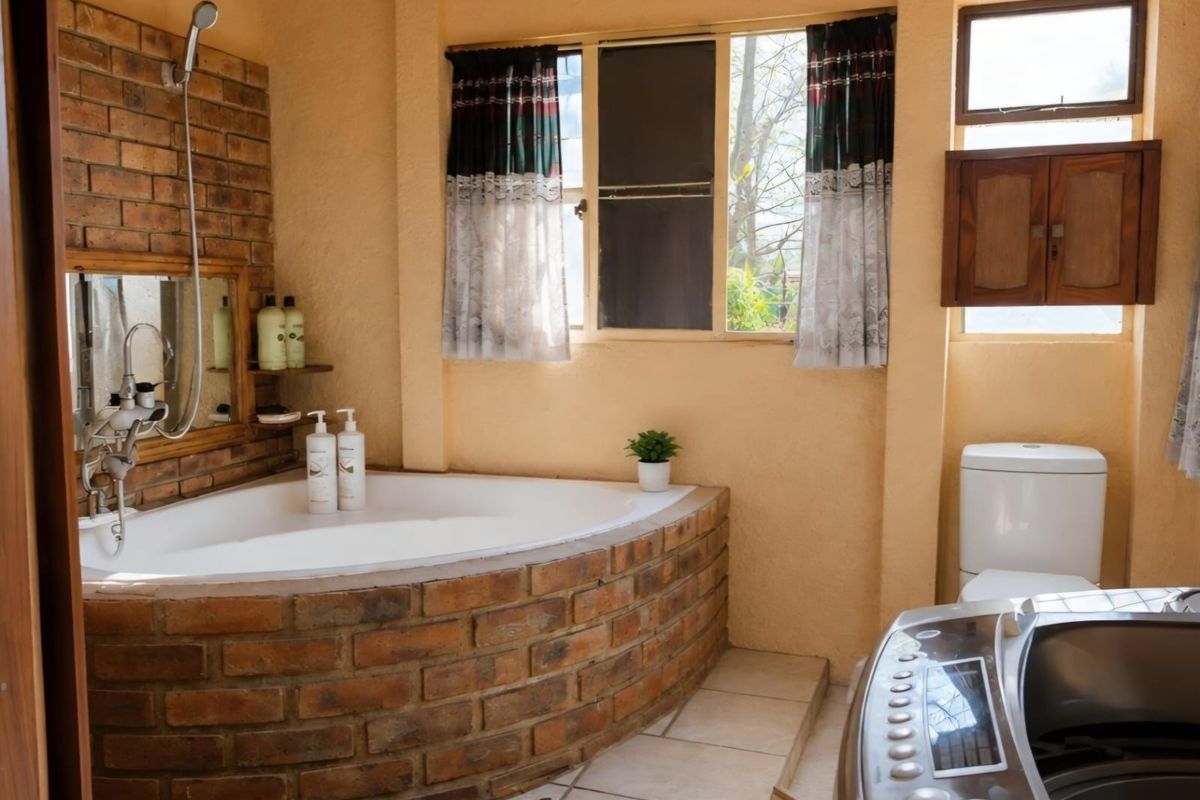 A rustic-style bathroom featuring a unique brick-clad corner bathtub, exposed brick accents, tiled flooring, and a built-in wooden wall cabinet.