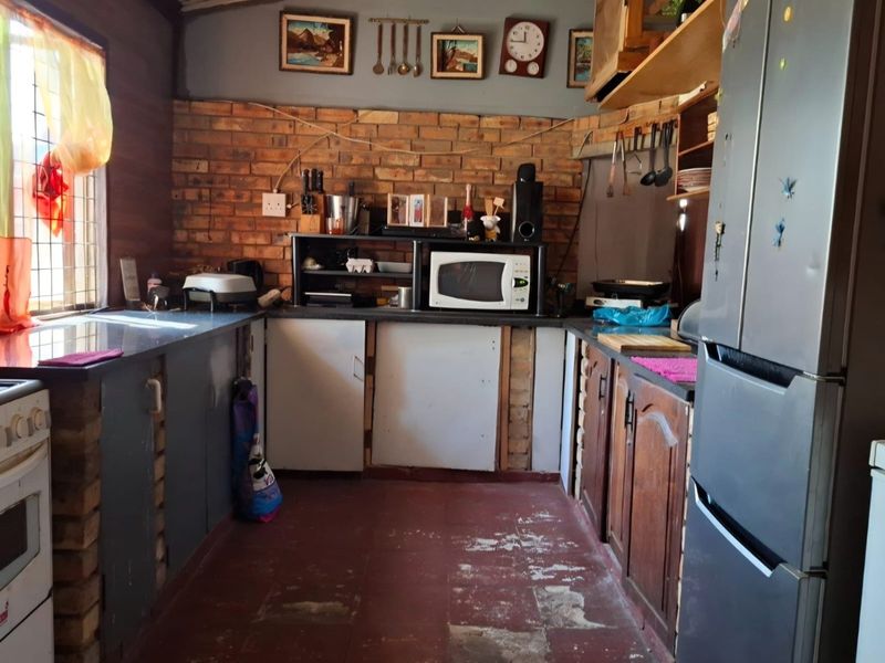 A rustic kitchen featuring exposed brick walls, built-in cabinetry, and a tiled floor. The space offers a functional layout with integrated appliances.