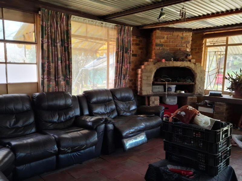 A rustic enclosed patio area featuring a built-in brick fireplace, corrugated metal ceiling, and large windows overlooking the garden.